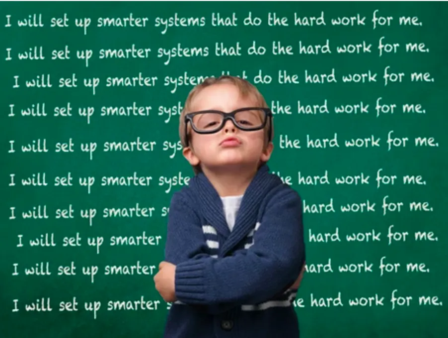 A boy with a spectacles standing in front of a black board and the text on black board is as follow : I will set up smarter systems that do the hardwork for me